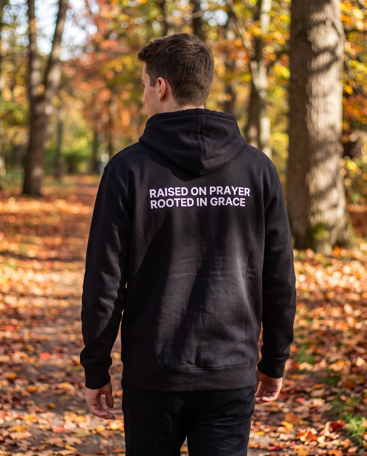 Back of a black Raised on Prayer. Rooted in Grace Christian hoodie showing the large back print
