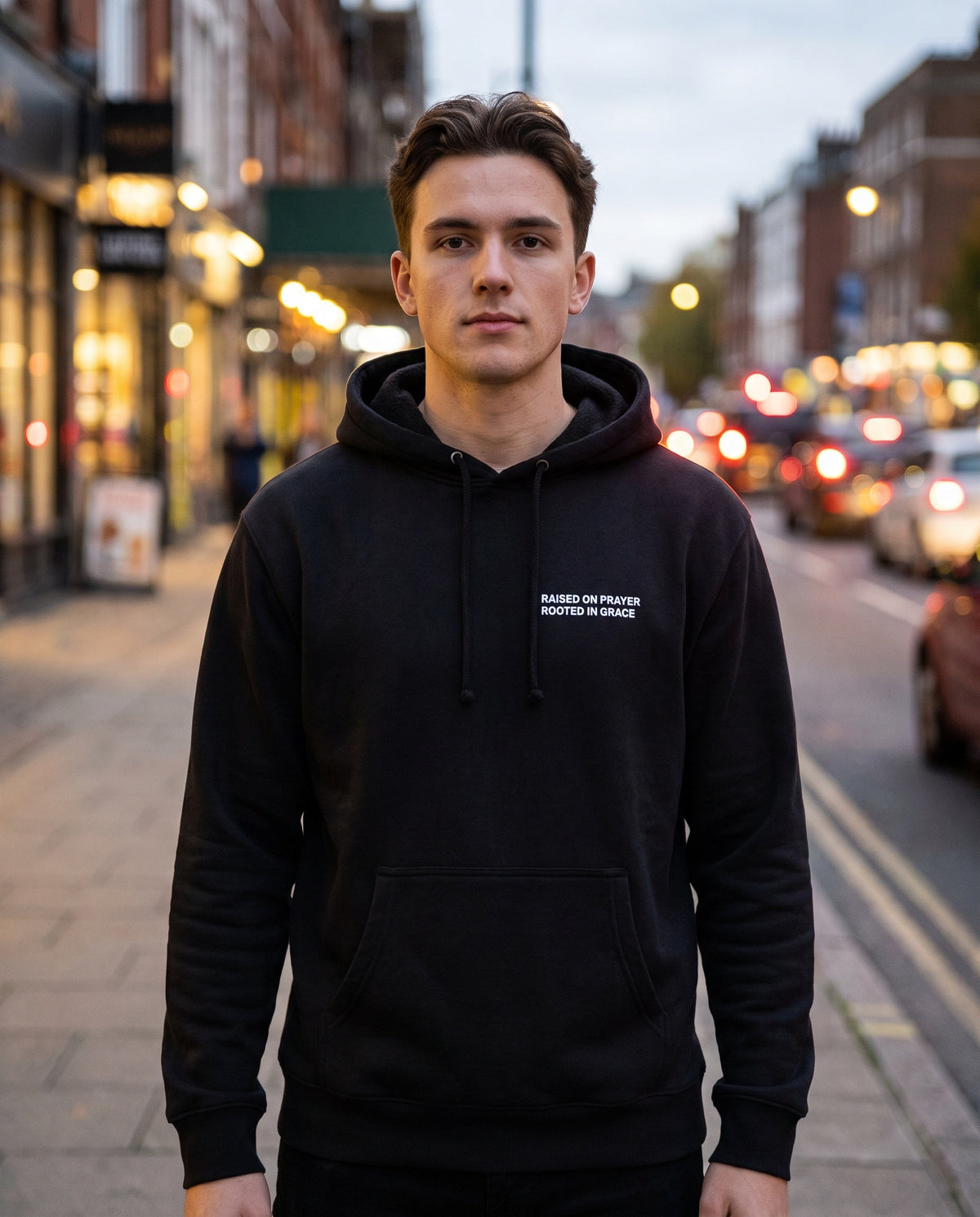 Man wearing a black Raised on Prayer. Rooted in Grace Christian hoodie, chest print