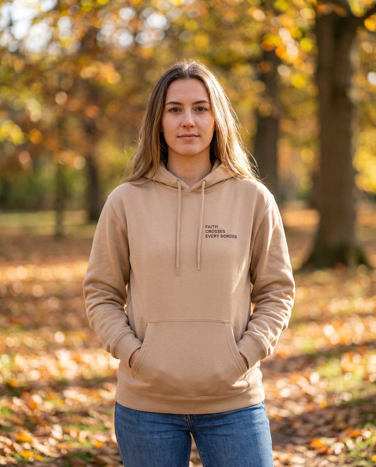 Woman wearing a sandstone Faith Crosses Every Border Christian hoodie, chest print