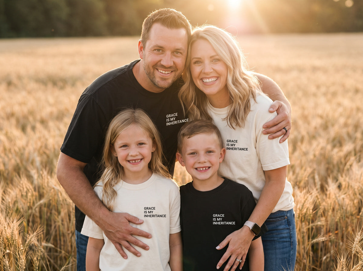 Family wearing matching Grace Is My Inheritance Christian t-shirts in black and ivory, golden-hour wheat field