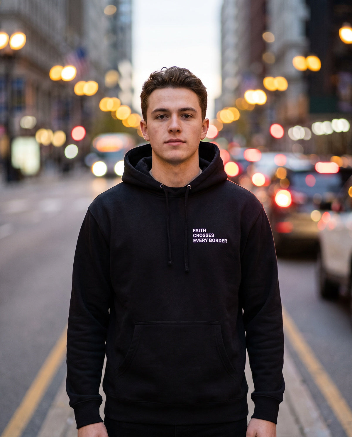 Man wearing a black Faith Crosses Every Border Christian hoodie, chest print