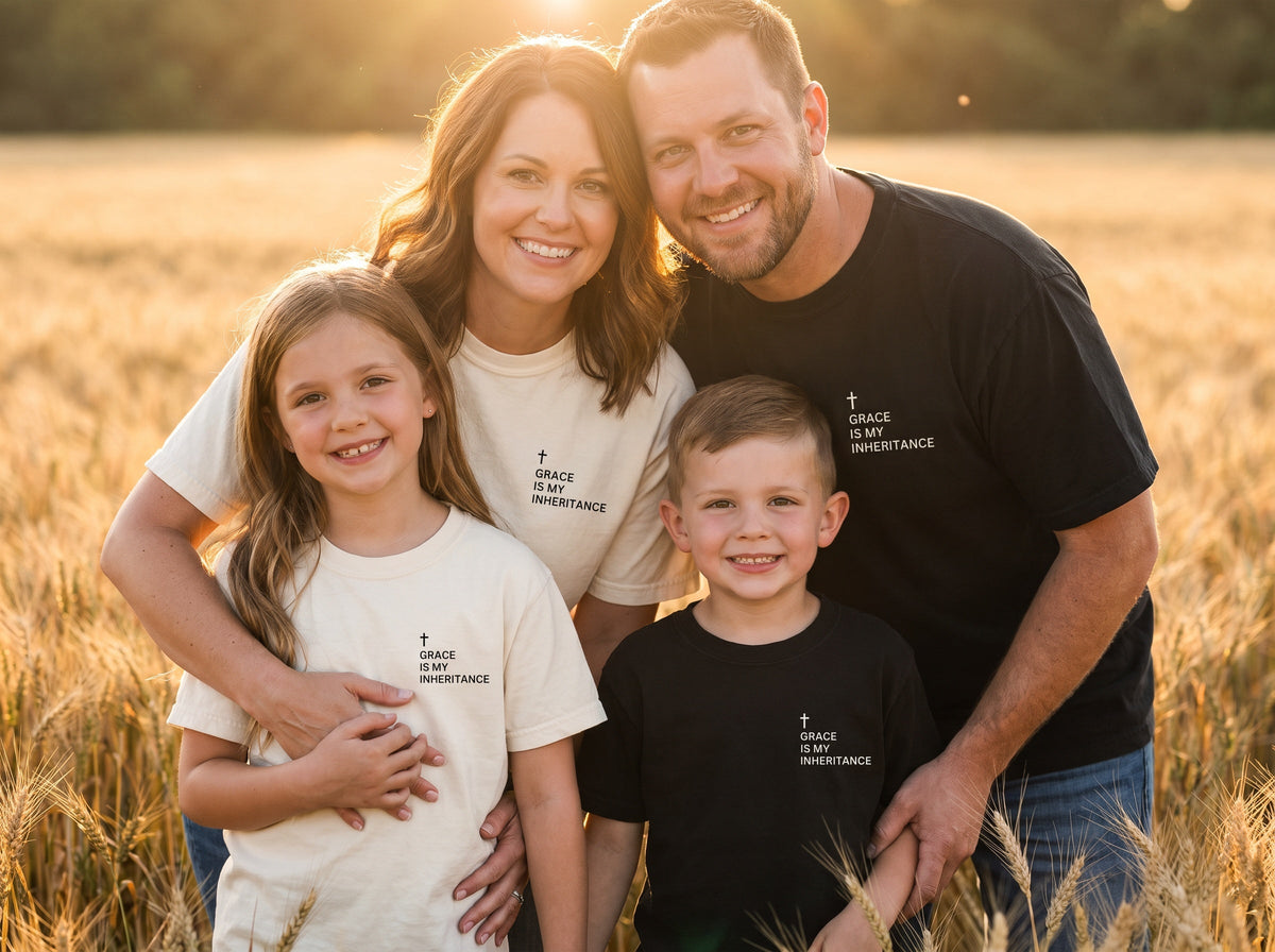 Family wearing matching Grace Is My Inheritance Cross Edition Christian t-shirts in black and ivory, golden-hour wheat field