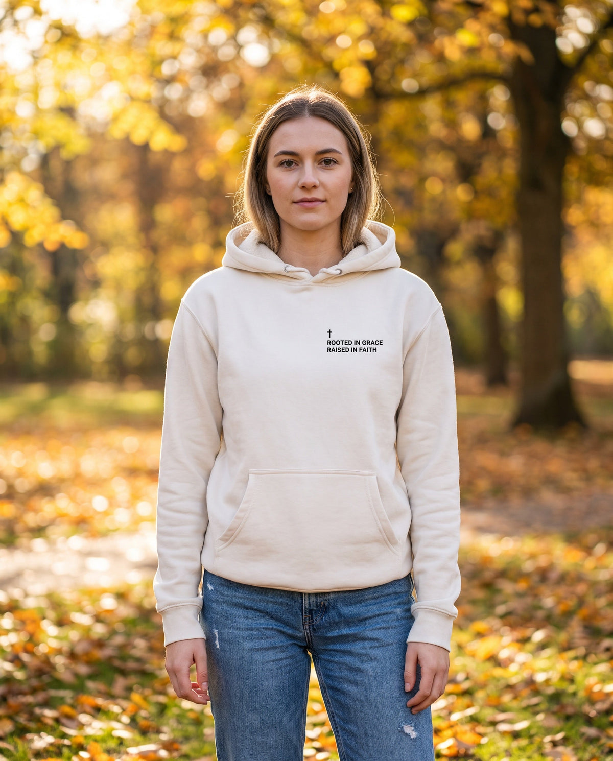 Woman wearing a bone Rooted in Grace. Raised in Faith Cross Edition Christian hoodie with cross chest print