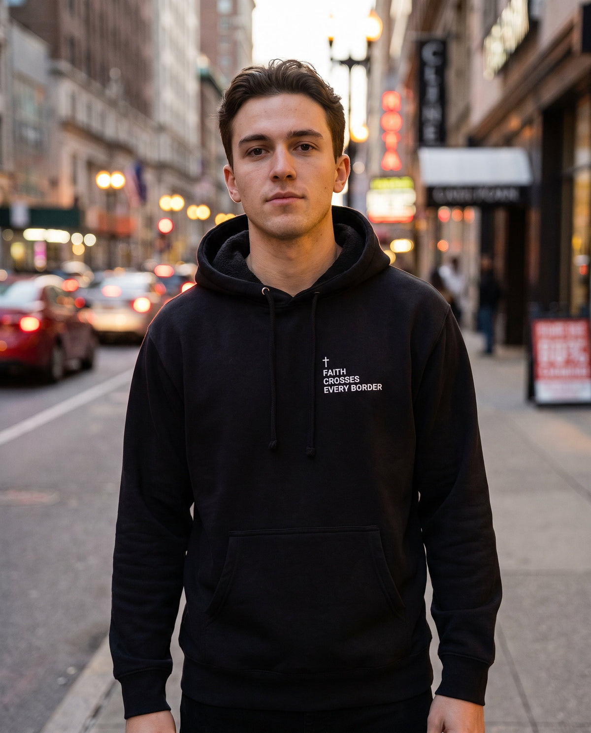 Man wearing a black Faith Crosses Every Border Cross Edition Christian hoodie with cross chest print