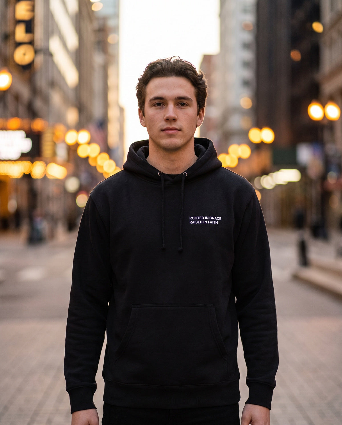 Man wearing a black Rooted in Grace. Raised in Faith Christian hoodie, chest print