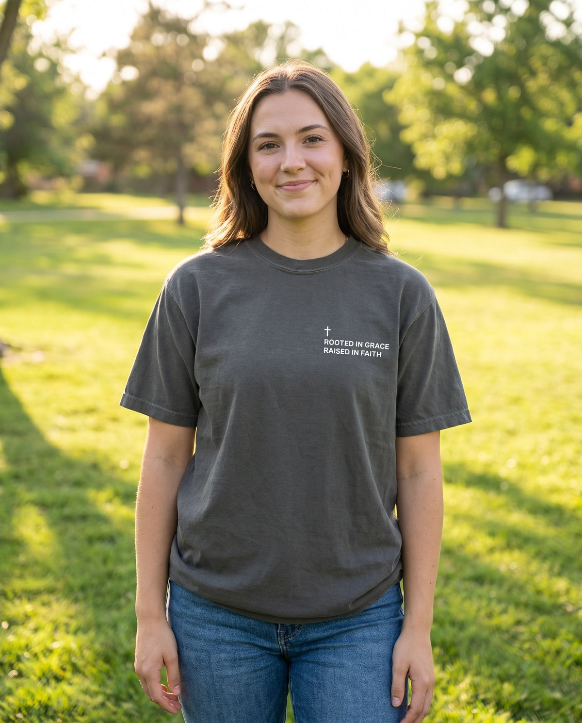Woman wearing a pepper Rooted in Grace. Raised in Faith Cross Edition Christian t-shirt with cross chest print