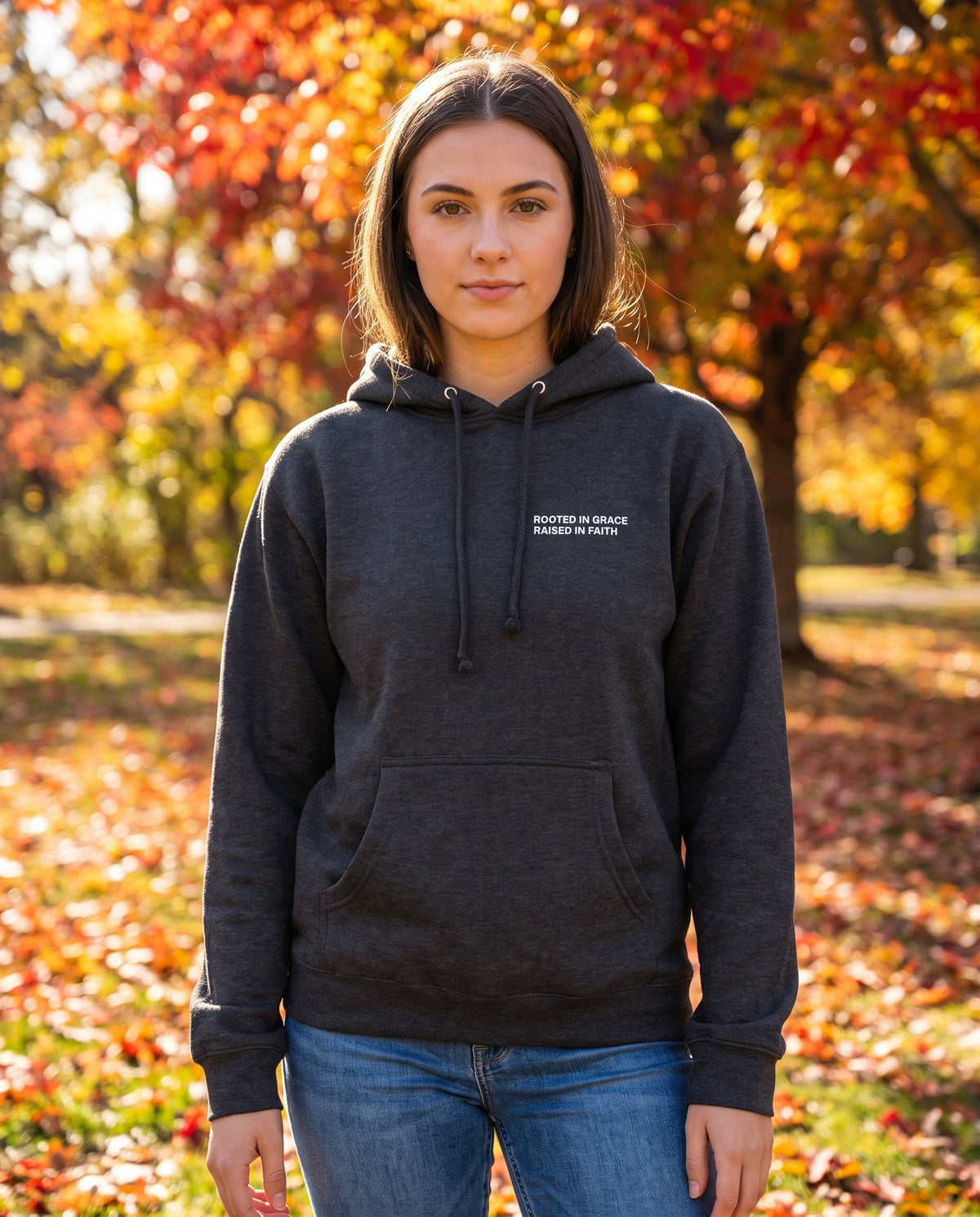 Woman wearing a charcoal Rooted in Grace. Raised in Faith Christian hoodie, chest print