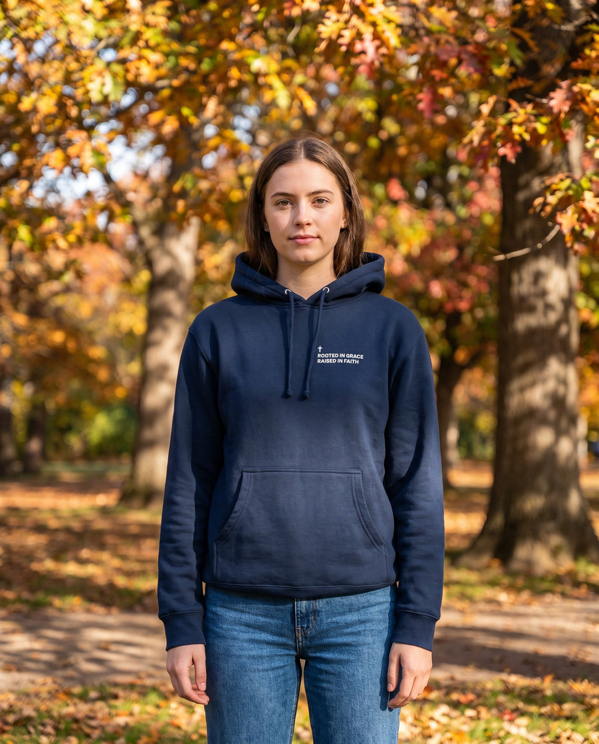 Woman wearing a navy Rooted in Grace. Raised in Faith Cross Edition Christian hoodie with cross chest print