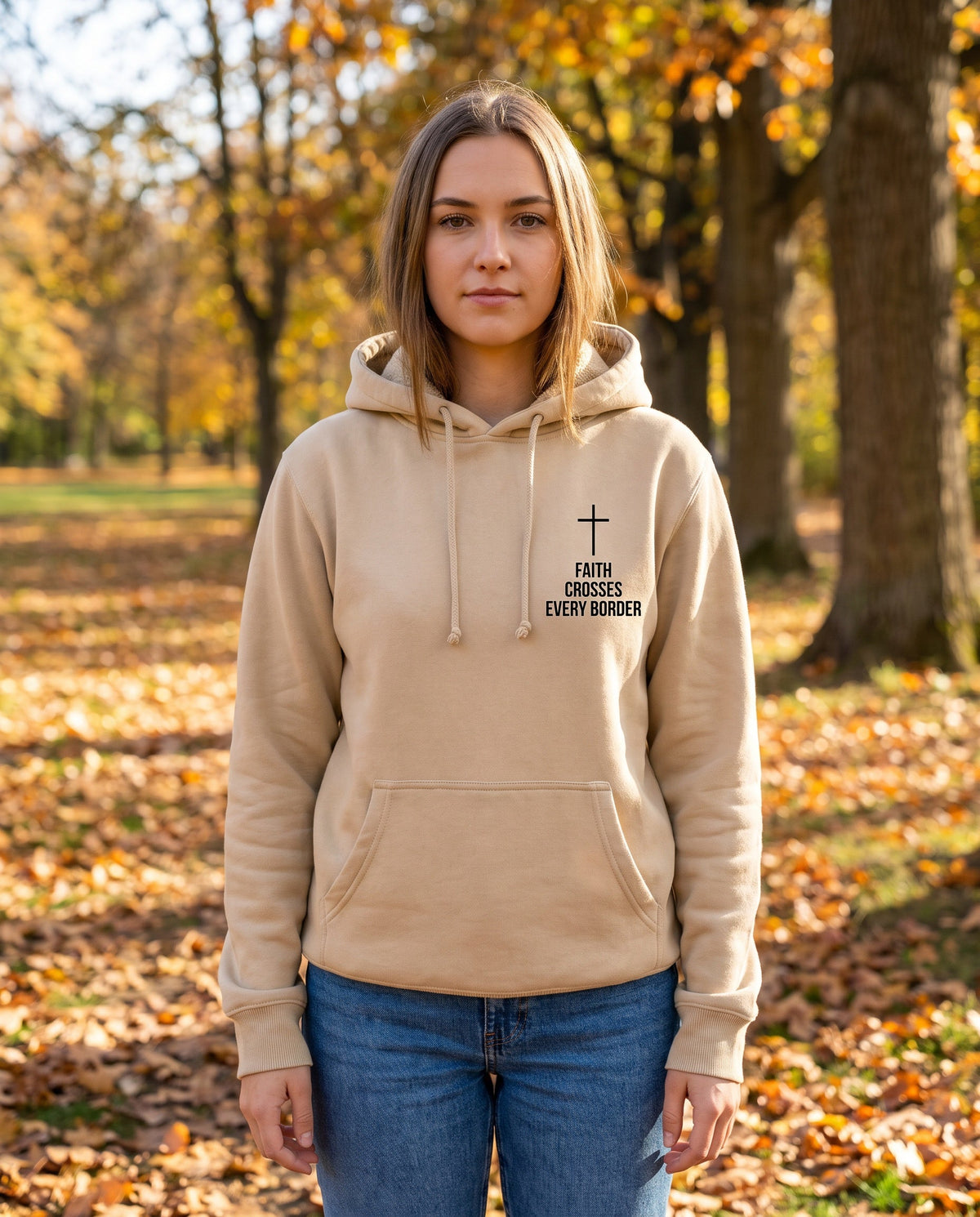 Woman wearing a sandstone Faith Crosses Every Border Cross Edition Christian hoodie with cross chest print