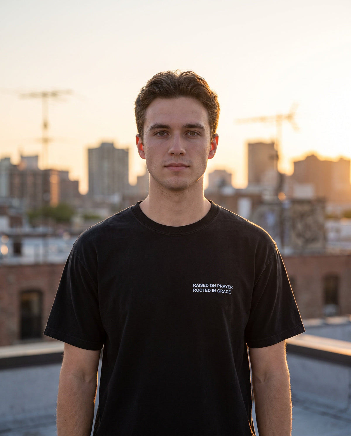 Man wearing a black Raised on Prayer. Rooted in Grace Christian t-shirt, chest print